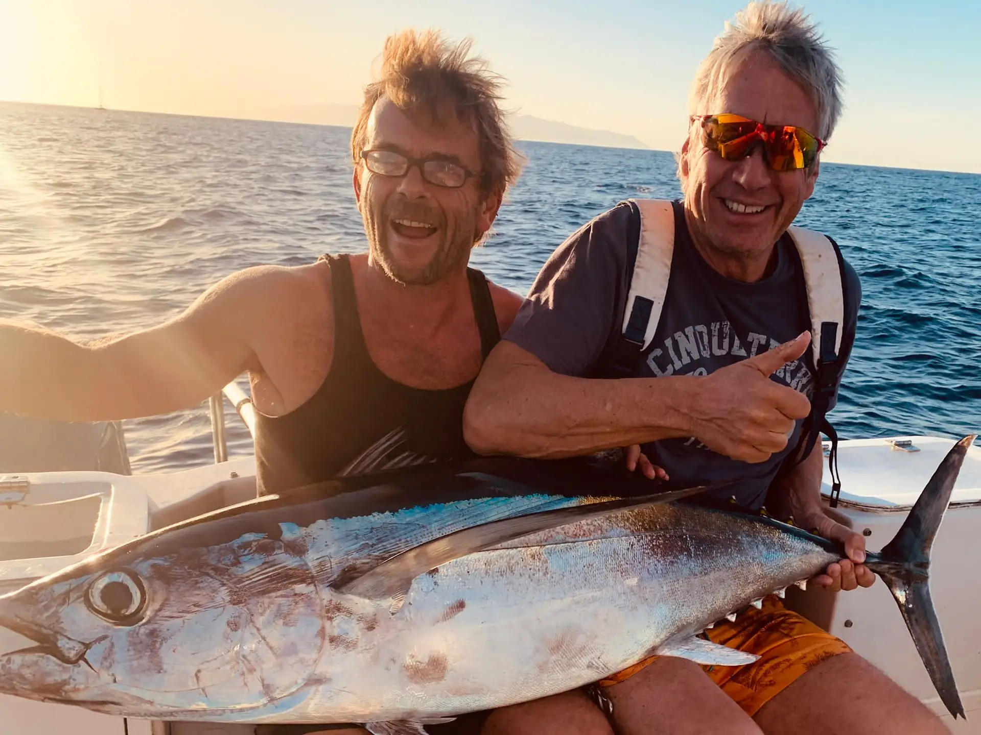 Two happy anglers holding a fresh tuna at sunset aboard a Tenerife fishing charter